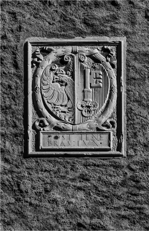 Stone relief of a historical coat of arms featuring a heraldic eagle on the left and a vertical key on the right, mounted on a textured building facade.
